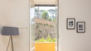 Une pièce dotée d’une porte vitrée donnant sur un balcon qui offre une vue sur un mur de briques et sur la verdure. Deux tableaux encadrés ornent le mur.