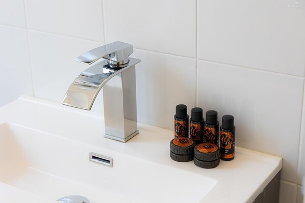 Un lavabo de salle de bain avec un robinet moderne et quatre flacons de produits capillaires.