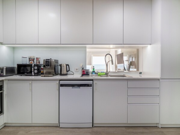 Une cuisine moderne avec des meubles blancs, un lave-vaisselle, une machine à café, un grille-pain et une bouilloire.