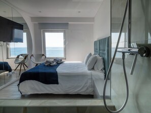 Een moderne hotelkamer met een bed, een televisie, een raam met uitzicht op zee en een douche.