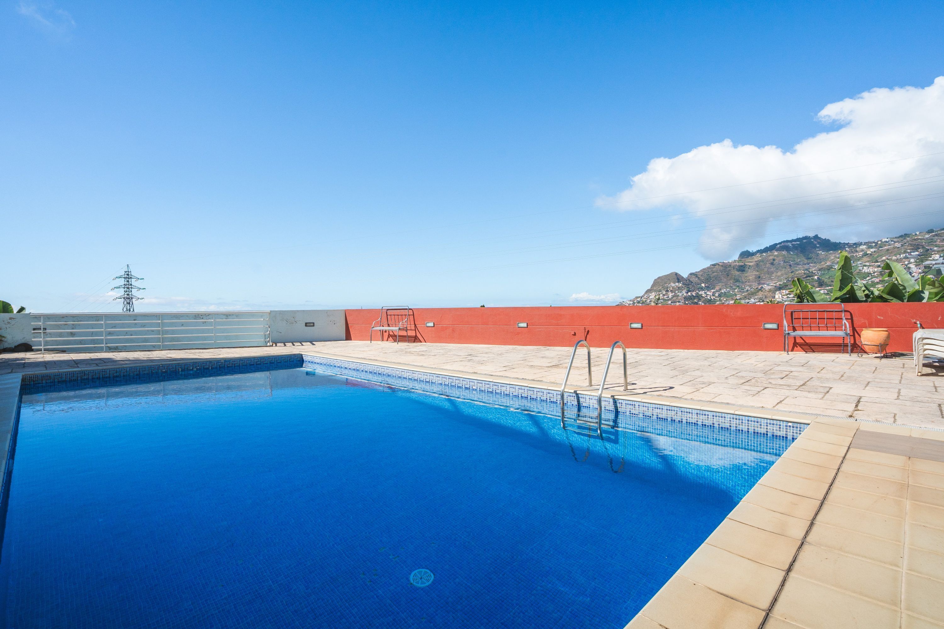 A rectangular swimming pool with clear blue water, surrounded by a red wall and a tiled deck area.