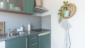 A kitchen with teal cabinets, a stainless steel sink, and a dish drying rack with a plant. - Pitanga by Atlantic Holiday (Camara de Lobos)