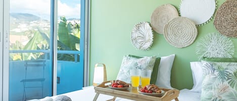 A hotel room with a balcony, a bed with a wooden tray, pillows, and a view of the city.