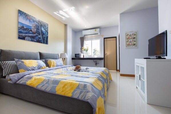 A bedroom with a bed, a TV, a desk, and a window.