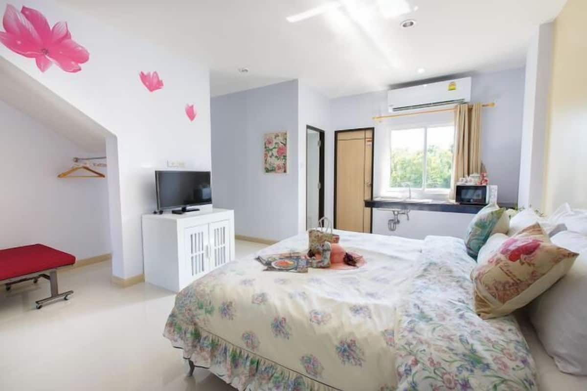 A bedroom with a bed, a TV, a desk, and a window.