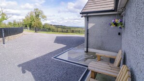A covered outdoor area with a gravel floor, wooden benches, and a wall-mounted flower pot. - Molly's Cottage (Enniskillen)