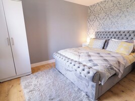 A bedroom with a tufted headboard, a patterned bedspread, and a fluffy rug.