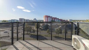 Een balkon met uitzicht op een stadsbeeld, een grote airconditioning en een gaas beveiligingshek.