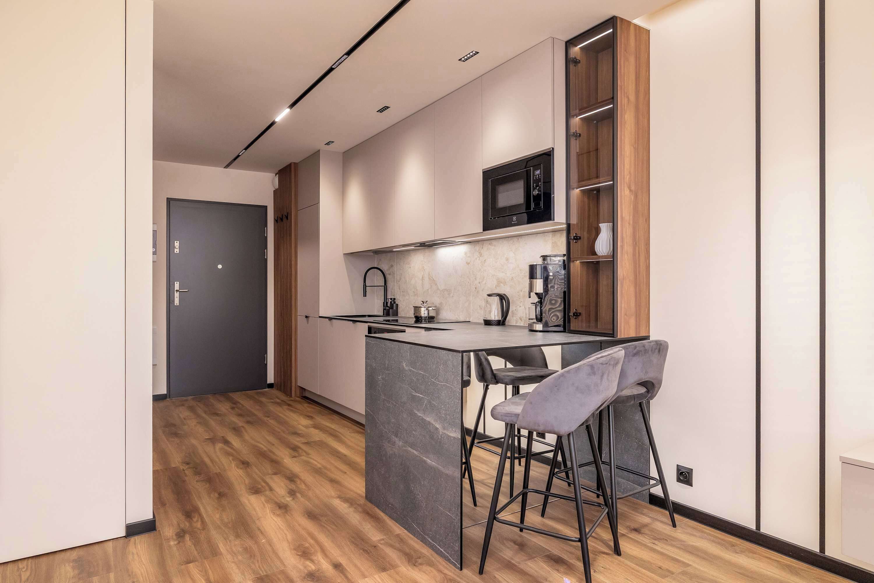 A modern kitchen with a marble island, bar stools, a microwave, and wooden cabinets.