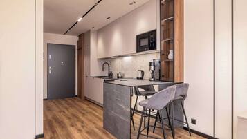 A modern kitchen with a marble island, bar stools, a microwave, and wooden cabinets.