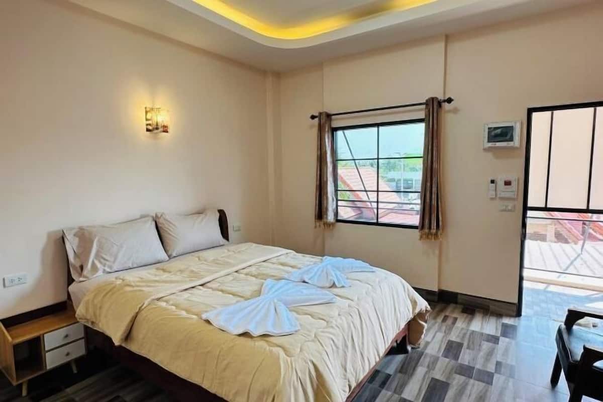 A hotel room with a bed, a bedside table, a window with curtains, and a view of the outside.