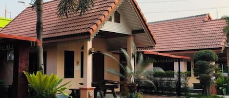 A two-story building with a red-tiled roof, a covered porch, and a small garden area with palm trees.