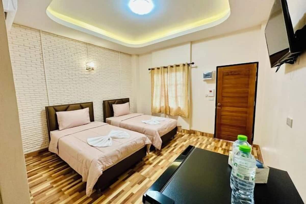 A hotel room with two beds, a wooden floor, a flat-screen TV, and a table with water bottles.