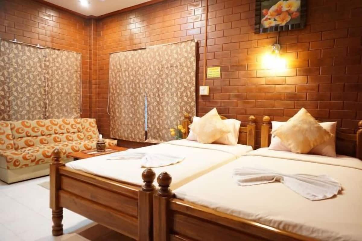 A hotel room with a brick wall, a sofa, two beds, and a wall-mounted light.