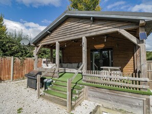A wooden cabin with a covered porch, outdoor seating, and a small patio area. - Willow Cottage (Romsey)