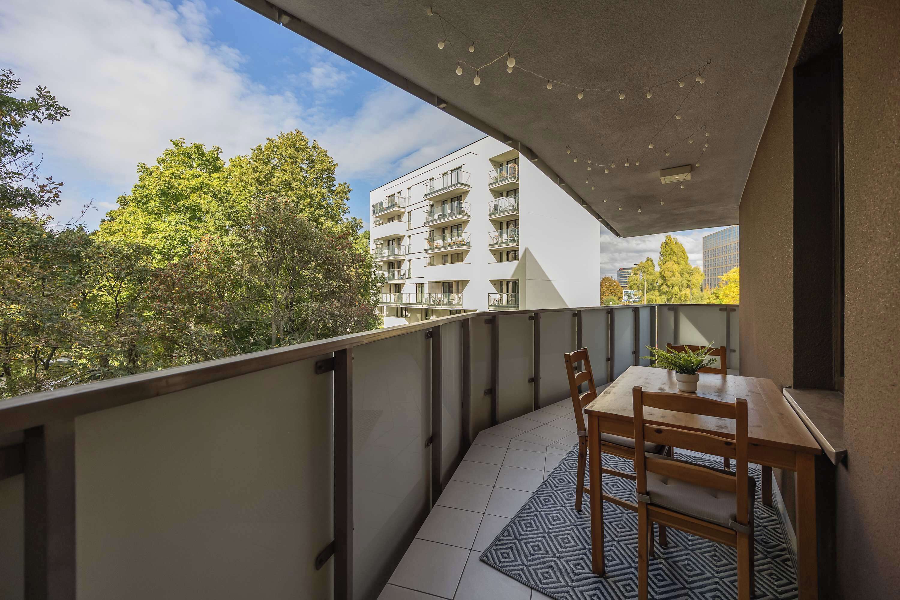 Un balcon avec une table et des chaises, une plante en pot et un tapis à motifs.