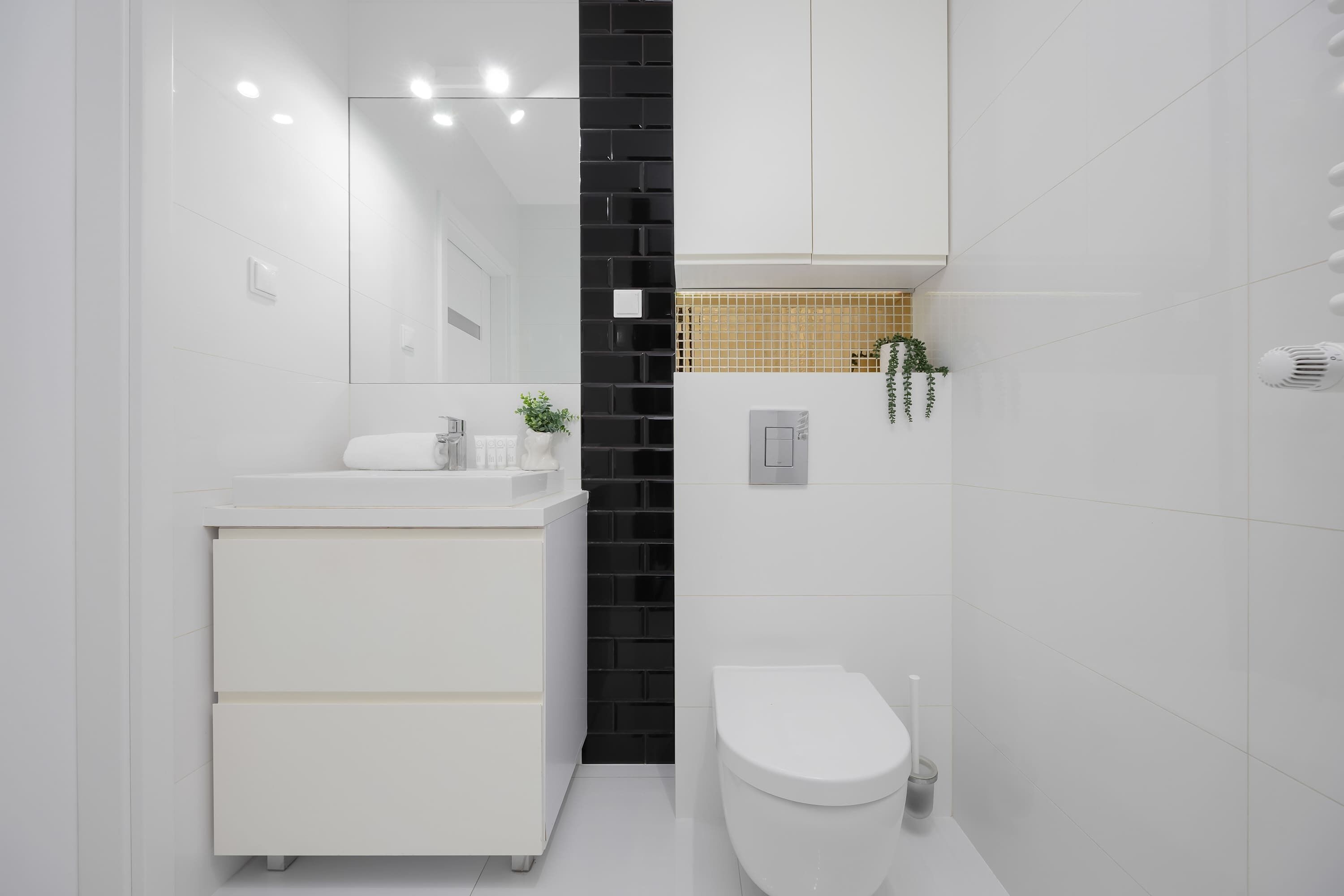 A modern bathroom with a white vanity, a black accent wall, a toilet, and a mirror.