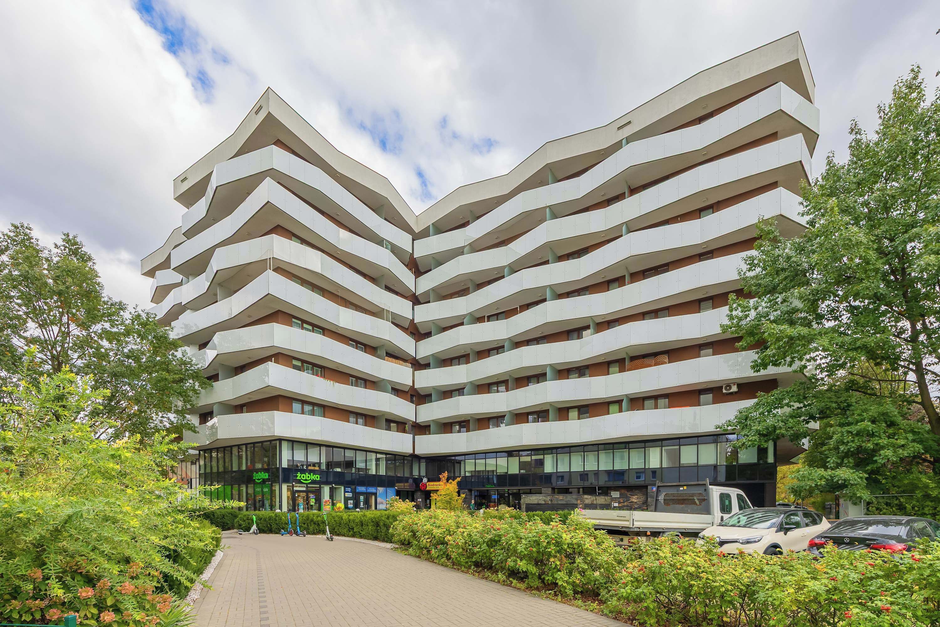 Un edificio de varios pisos con un diseño arquitectónico en zigzag, con balcones y un patio central con vegetación.