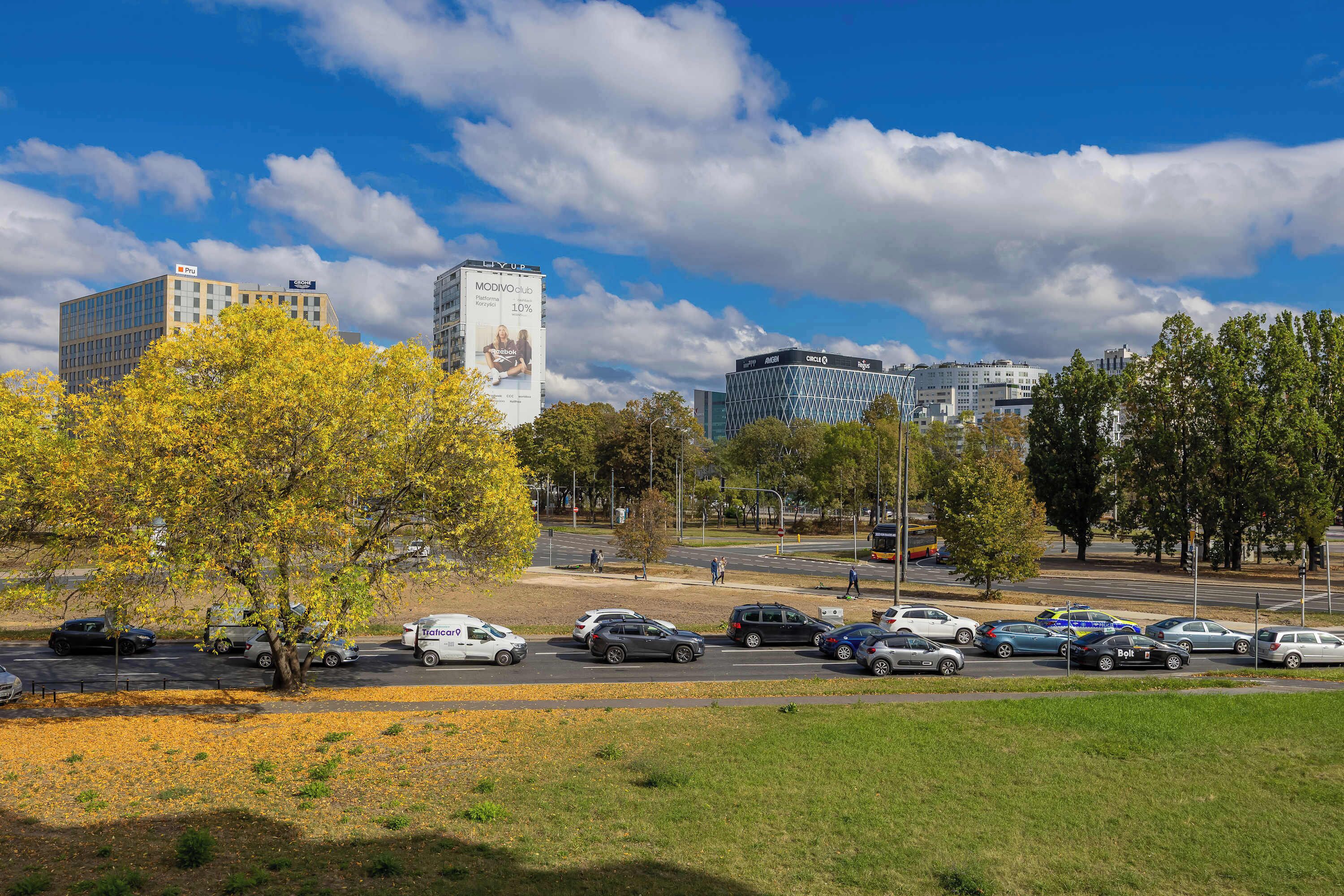 A parking lot with multiple cars and a few pedestrians.