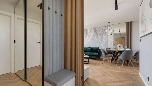 A modern living room with a sofa, a dining table with chairs, and a large mirror.