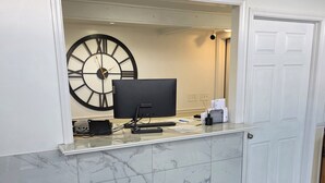 Un comptoir d’accueil avec un ordinateur, un clavier et une horloge au mur.