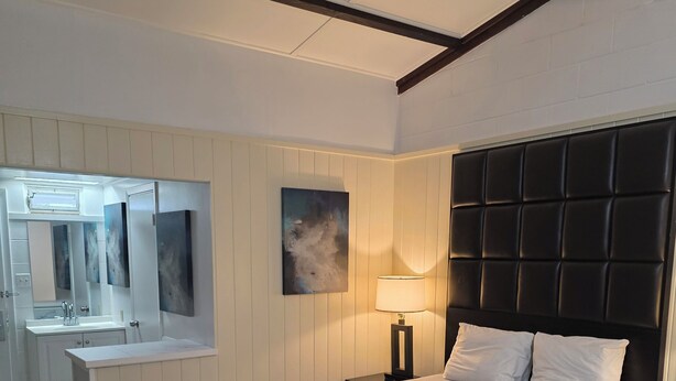 Une chambre à coucher avec un lit, une table de chevet, une lampe, un miroir et un tableau accroché au mur.