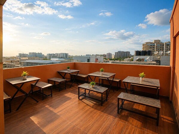 Une terrasse sur le toit, dotée d’un plancher en bois, de plusieurs tables et bancs, de plantes en pot et offrant une vue sur la ville.