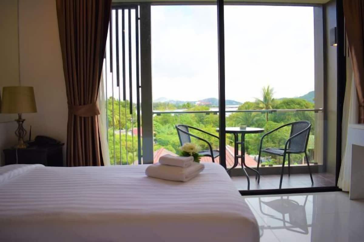 Ein Hotelzimmer mit einem großen Bett, einem Schreibtisch, einem Stuhl und einem Balkon mit Blick auf Grünflächen und Hügel.