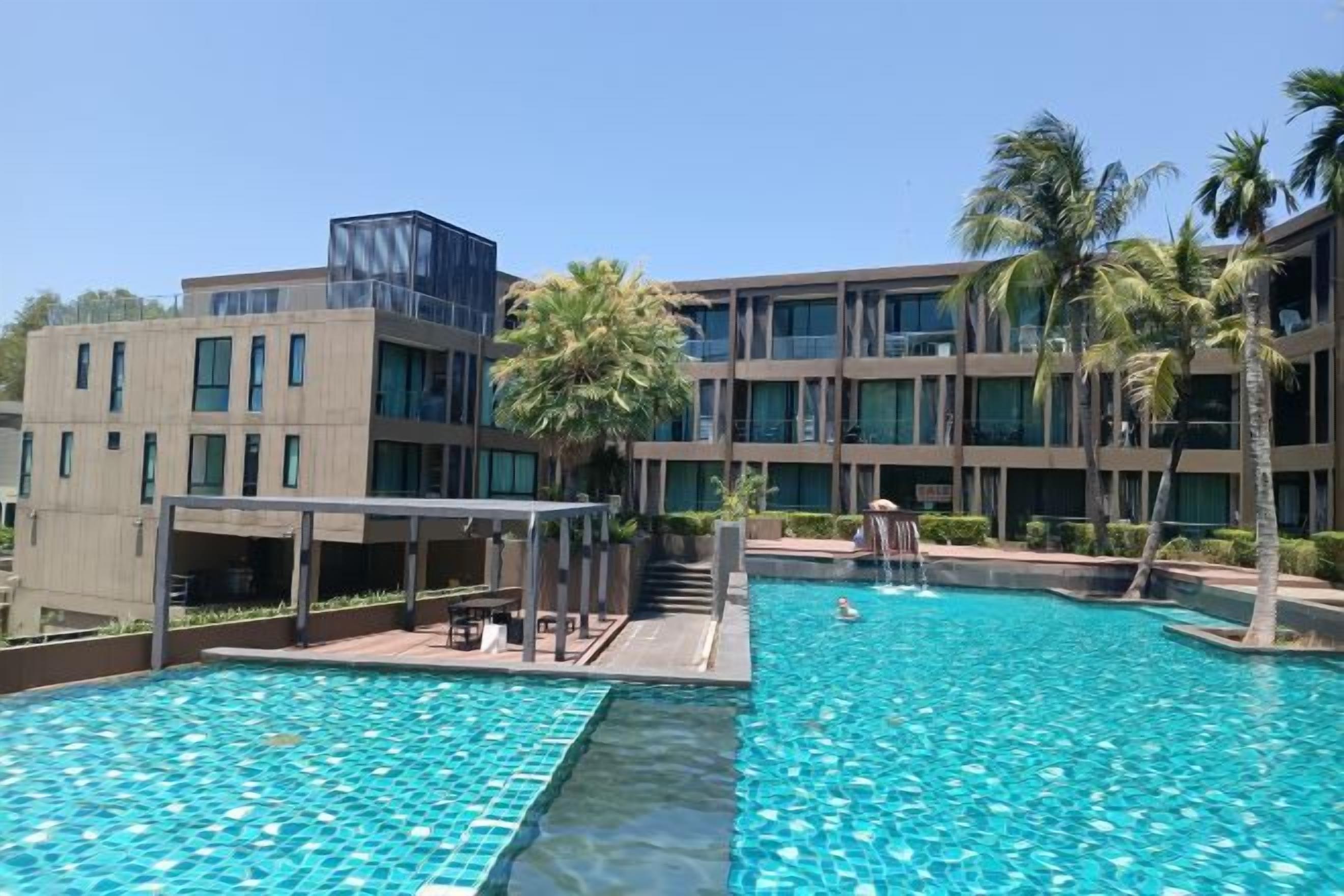 A swimming pool with a clear blue water surface, surrounded by a modern building with multiple floors and windows.