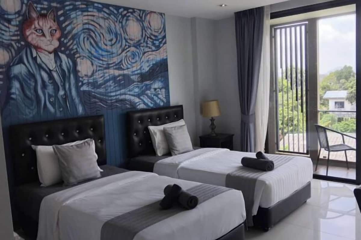 Ein Hotelzimmer mit zwei Betten, einem großen Gemälde an der Wand, einem Balkon mit Aussicht und einer Lampe auf einem Nachttisch.