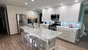 A modern kitchen with white cabinetry, a central island with stools, and a herringbone-patterned wooden floor.