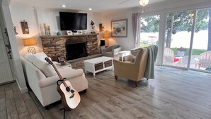 A spacious living room with a stone fireplace, a flat-screen TV, and a ceiling fan.