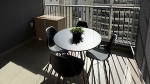 A balcony with a round table and chairs, a small potted plant, and a view of surrounding buildings. - On Jurupis (São Paulo)