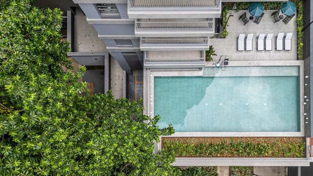 An aerial view of a modern building with a rooftop swimming pool surrounded by lounge chairs and umbrellas. - On Jurupis (São Paulo)