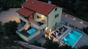 Ein zweistöckiges Haus mit Swimmingpool, Außenbereich zum Sitzen und einem roten Ziegeldach.