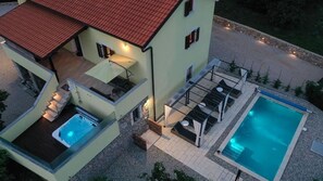 Una casa de dos pisos con piscina, mobiliario exterior y bañera de hidromasaje.