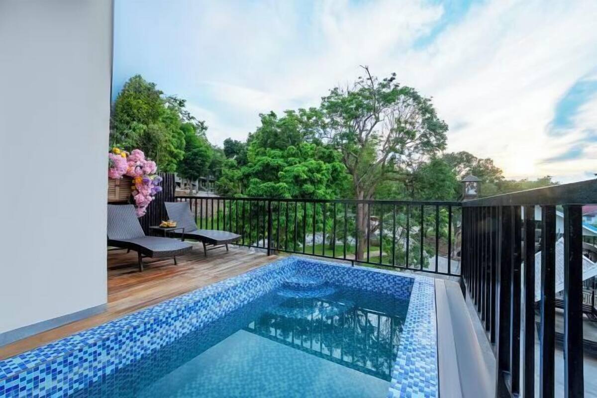 A rooftop pool with a tiled edge, surrounded by a wooden deck and black railing.