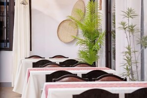 A dining area with tables set for guests, a potted plant, and decorative wall art. - Fu Er Man Hotel (Luang Prabang)