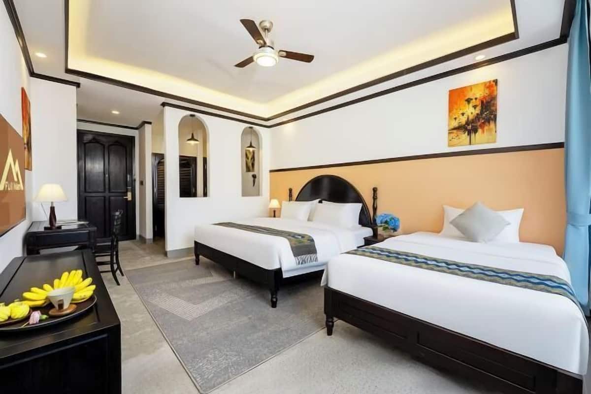 A hotel room with two beds, a desk with a lamp, a ceiling fan, and artwork on the walls.