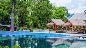 A pool area with a clear blue water surface, surrounded by lush greenery and thatched-roof structures. - Fu Er Man Hotel (Luang Prabang)
