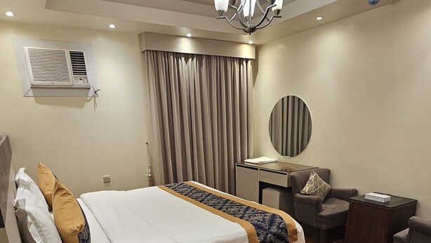 A hotel room with a bed, a desk, a chair, a mirror, and a ceiling fan. - Saad Palace for seviced apartments (Abha)