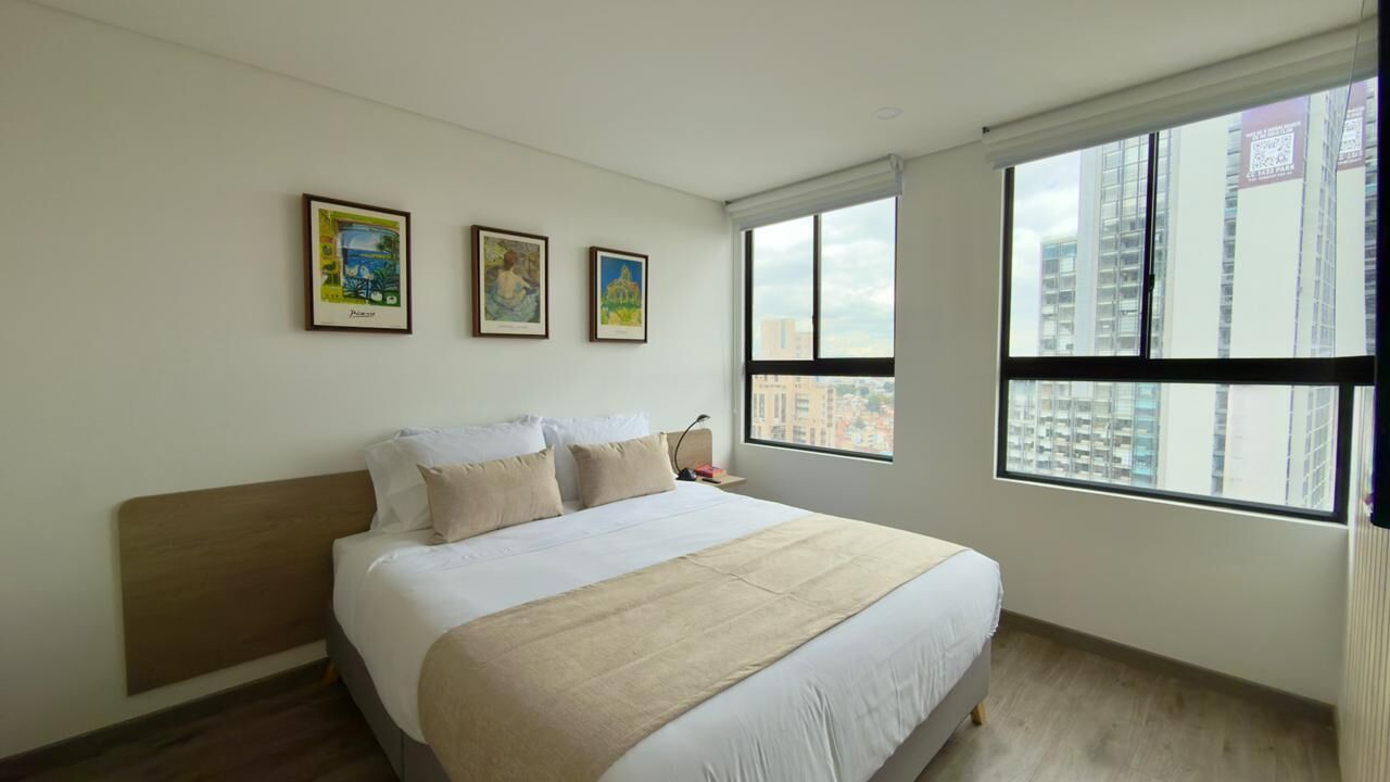 A bedroom with a large bed, a nightstand, and a window with a city view.