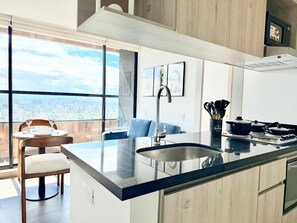 A modern kitchen with a large island, a dining area with a view, and a cityscape visible through large windows.