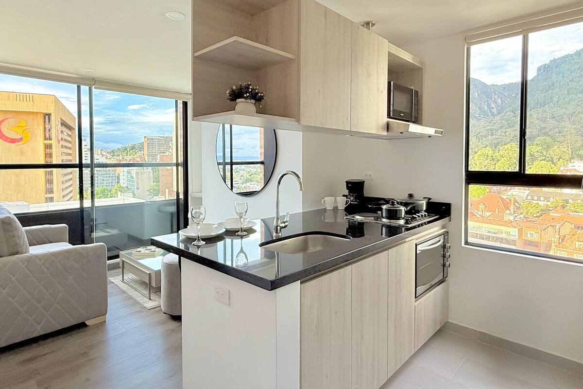 Une cuisine moderne dotée d’un îlot central, d’un four encastré et d’une grande fenêtre offrant une vue sur la ville.
