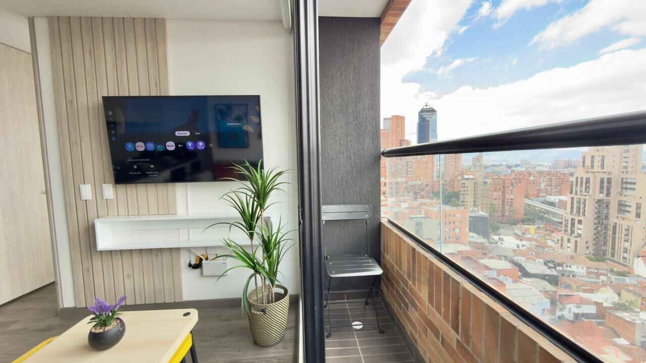 Un balcón con vista a la ciudad, un televisor de pantalla plana y dos plantas en macetas.