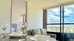 Une chambre d’h ôtel moderne avec une table à manger dressée pour deux personnes, un canapé et une grande fenêtre donnant sur la ville.