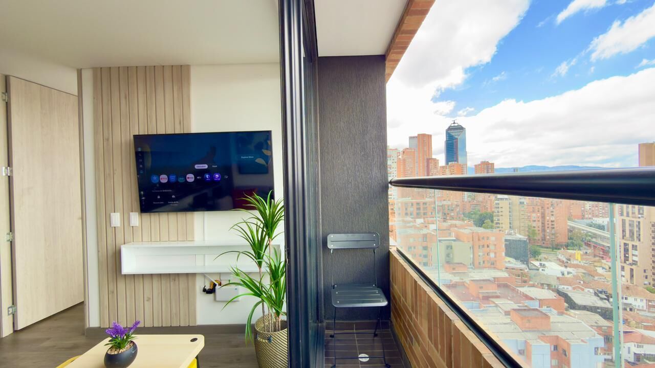 Un balcon avec un téléviseur, un pot de fleurs et une chaise.
