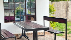 A patio with a wooden table and benches, a window, and a view of a garden. - Gem Villa Inn (Lesoma)