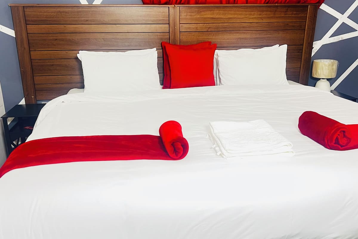 Un lit bien fait, avec du linge de lit blanc et rouge, une tête de lit en bois et un mur orné d’un motif géométrique.