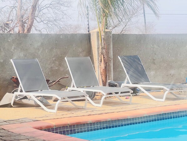 Zona de piscina con sillas de descanso y una pared de hormigón.